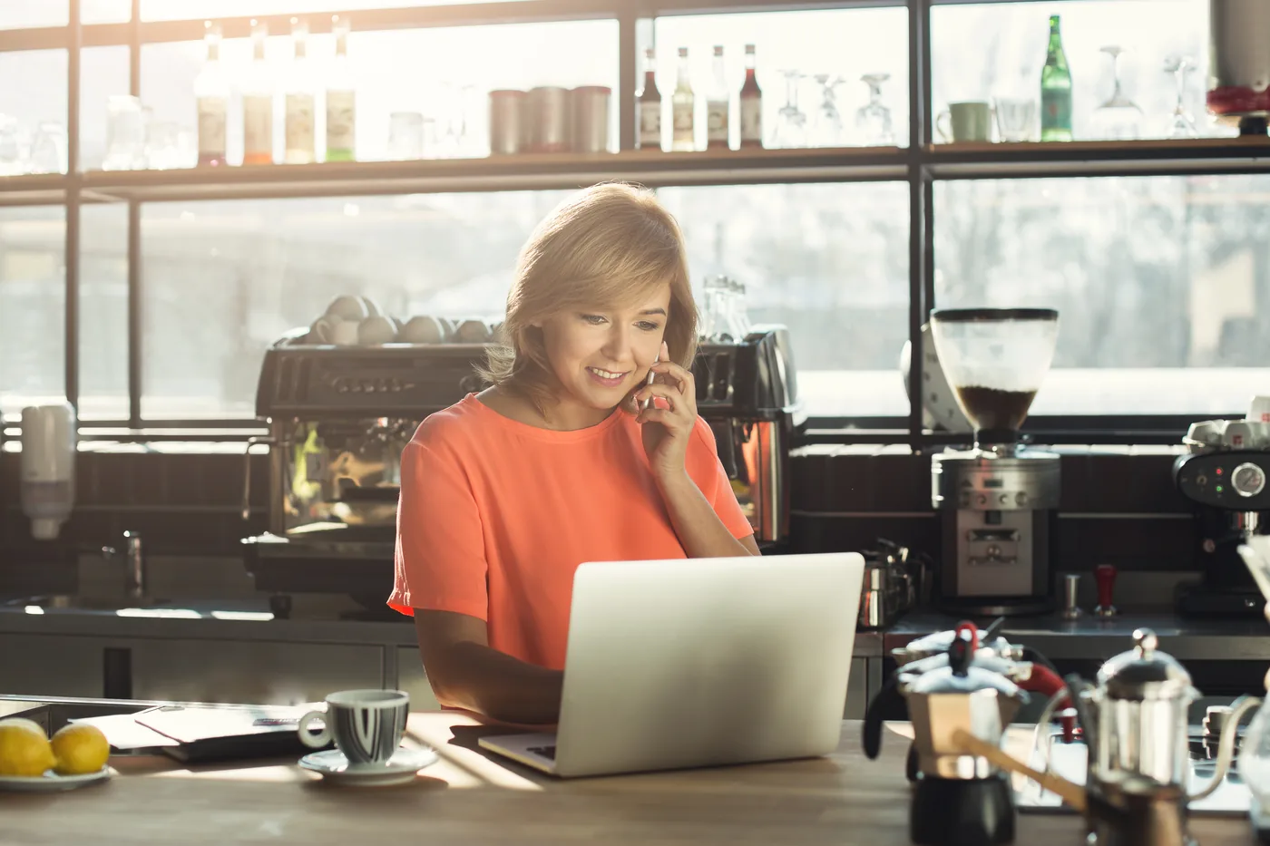 Dueña de una cafetería atendiendo pedidos desde su laptop y su teléfono
